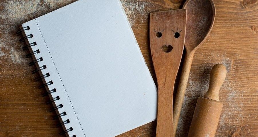 Open recipe book with wooden spoon, rolling pan and spatula  on wooden background, selective focus. Cooking course poster background - layout with free text space.