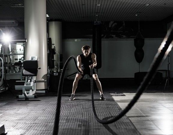 Fitness man working out with battle ropes at gym. Battle ropes fitness man at gym workout exercise fitted body. Fitness man training with battle rope in fitness club.