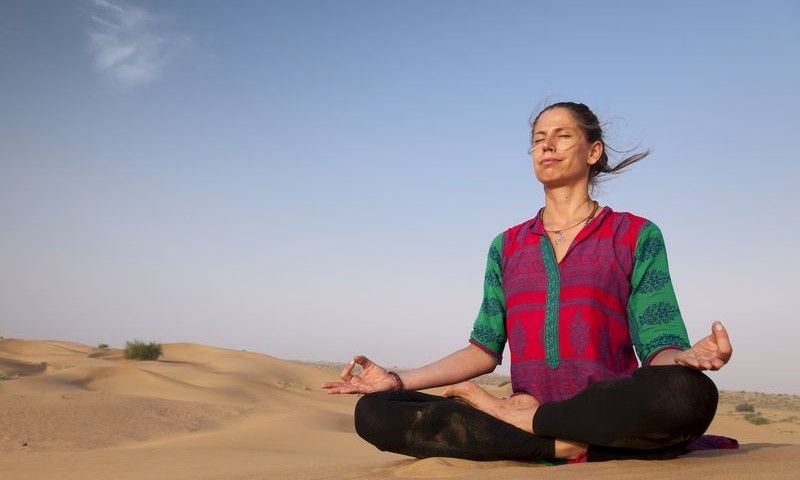 Young female practising yoga meditation on sand dune Jaisalmer, India
