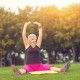 Woman with raised arms sitting. Lady with closed eyes outdoor. Concentrate and breathe deeply. Flexibility and health.