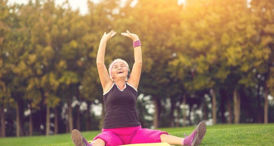 Woman with raised arms sitting. Lady with closed eyes outdoor. Concentrate and breathe deeply. Flexibility and health.