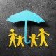 Paper cutout family of four under a blue paper umbrella