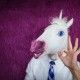 Freaky young man in comical mask stands on the purple background. Portrait of unusual manager. Funny unicorn in shirt and tie is showing gesture alright