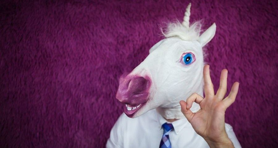 Freaky young man in comical mask stands on the purple background. Portrait of unusual manager. Funny unicorn in shirt and tie is showing gesture alright