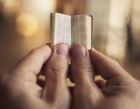 Two hands holding a very small Bible.